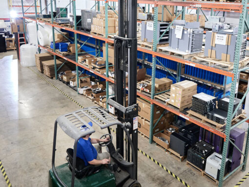 Forklift operator organizing stacked pallets of decommissioned server chassis in an IT asset disposition warehouse.